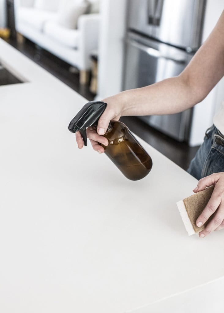 Woman cleaning kitchen cabinets with a multipurpose spray and sponge after purging kitchen items
